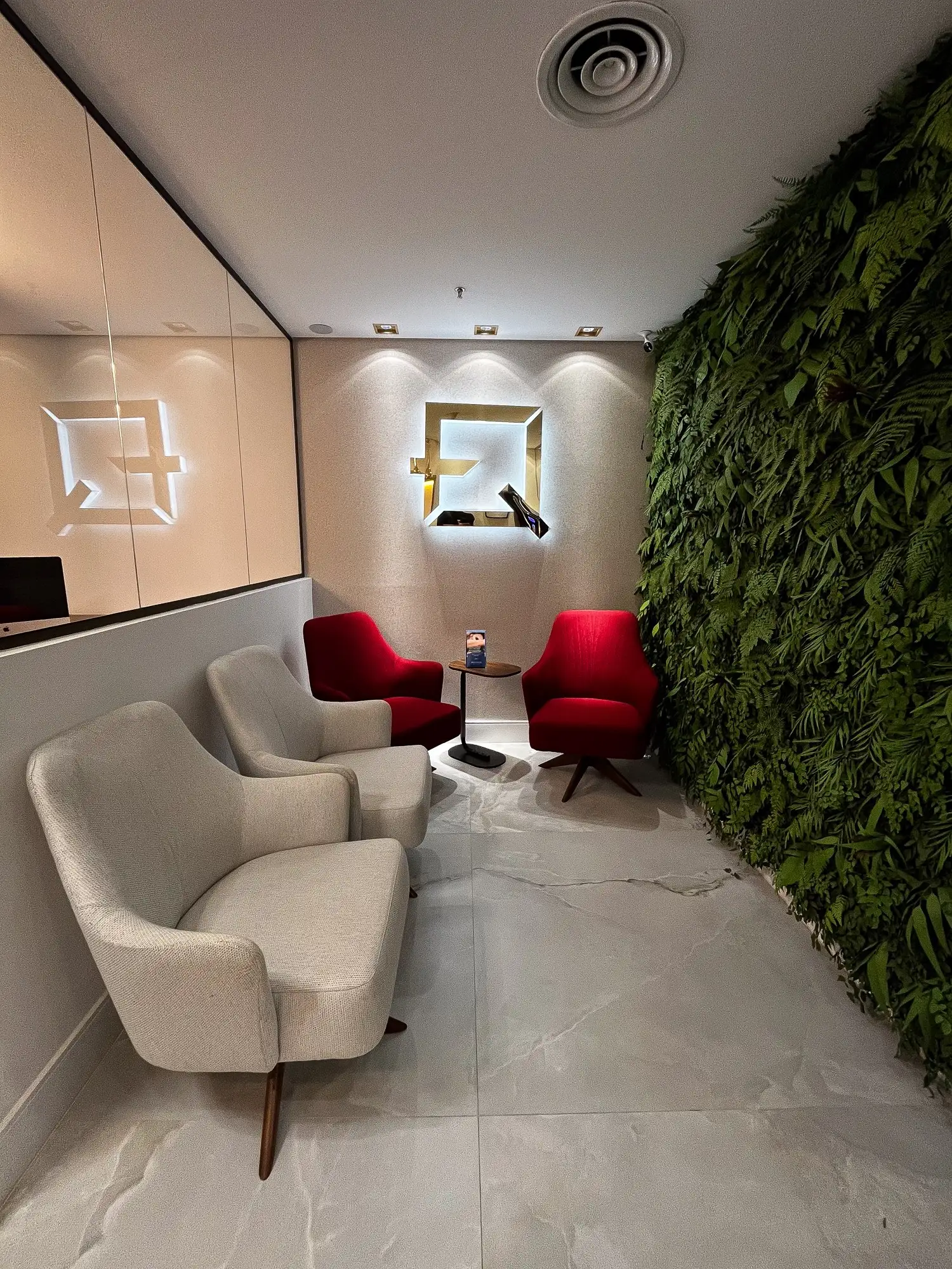 Sala de espera com poltronas, parede verde e o monograma FQ iluminado