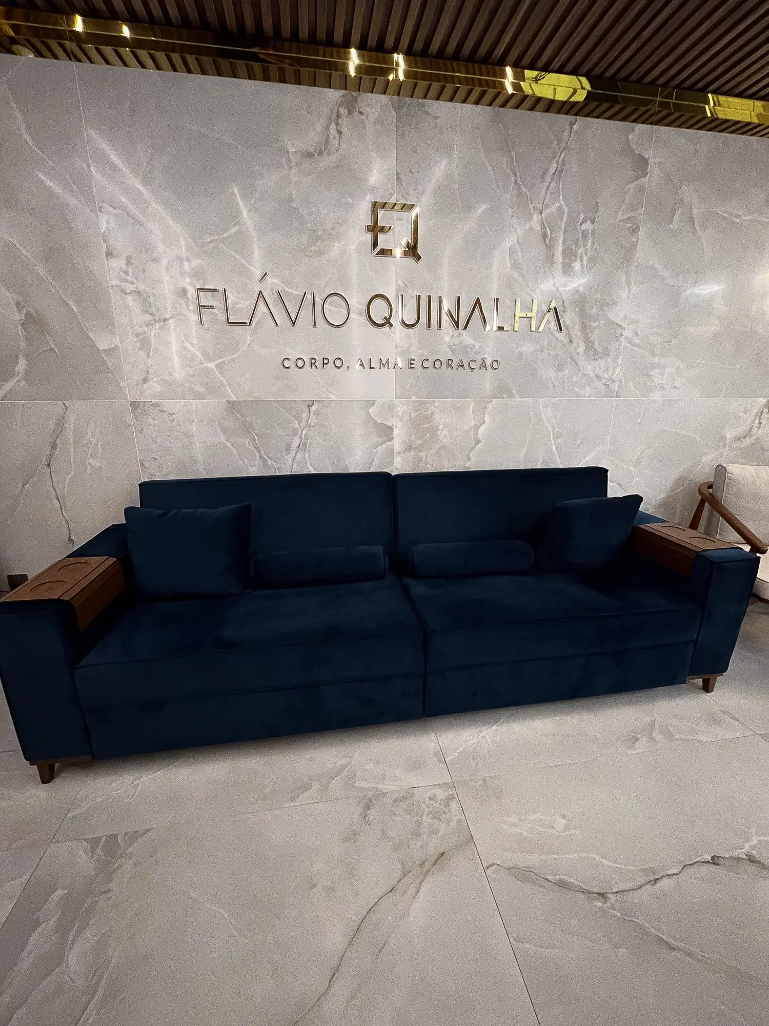 Recepção com sofá azul e o nome Flávio Quinalha na parede de mármore
